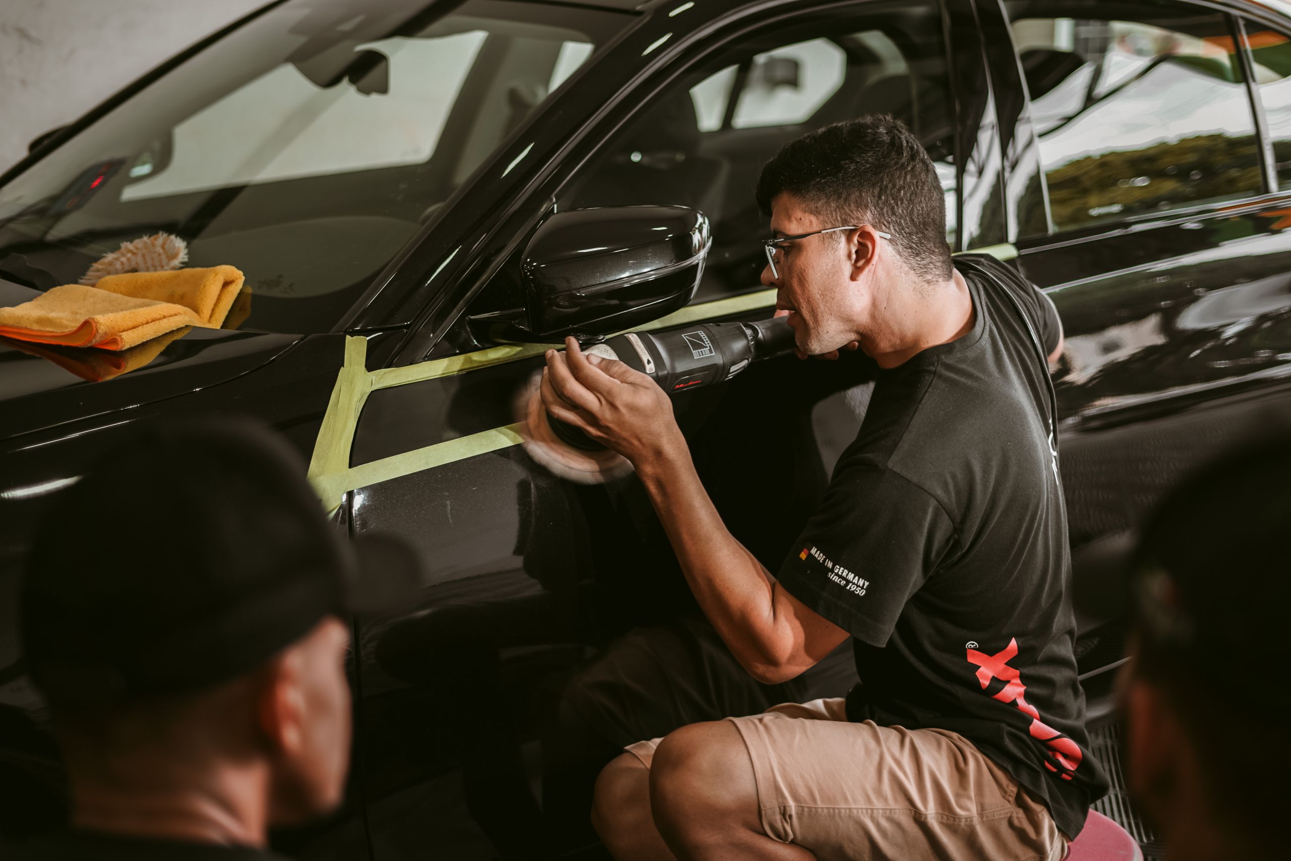 A technician masking and prepping a dark car door for paint
