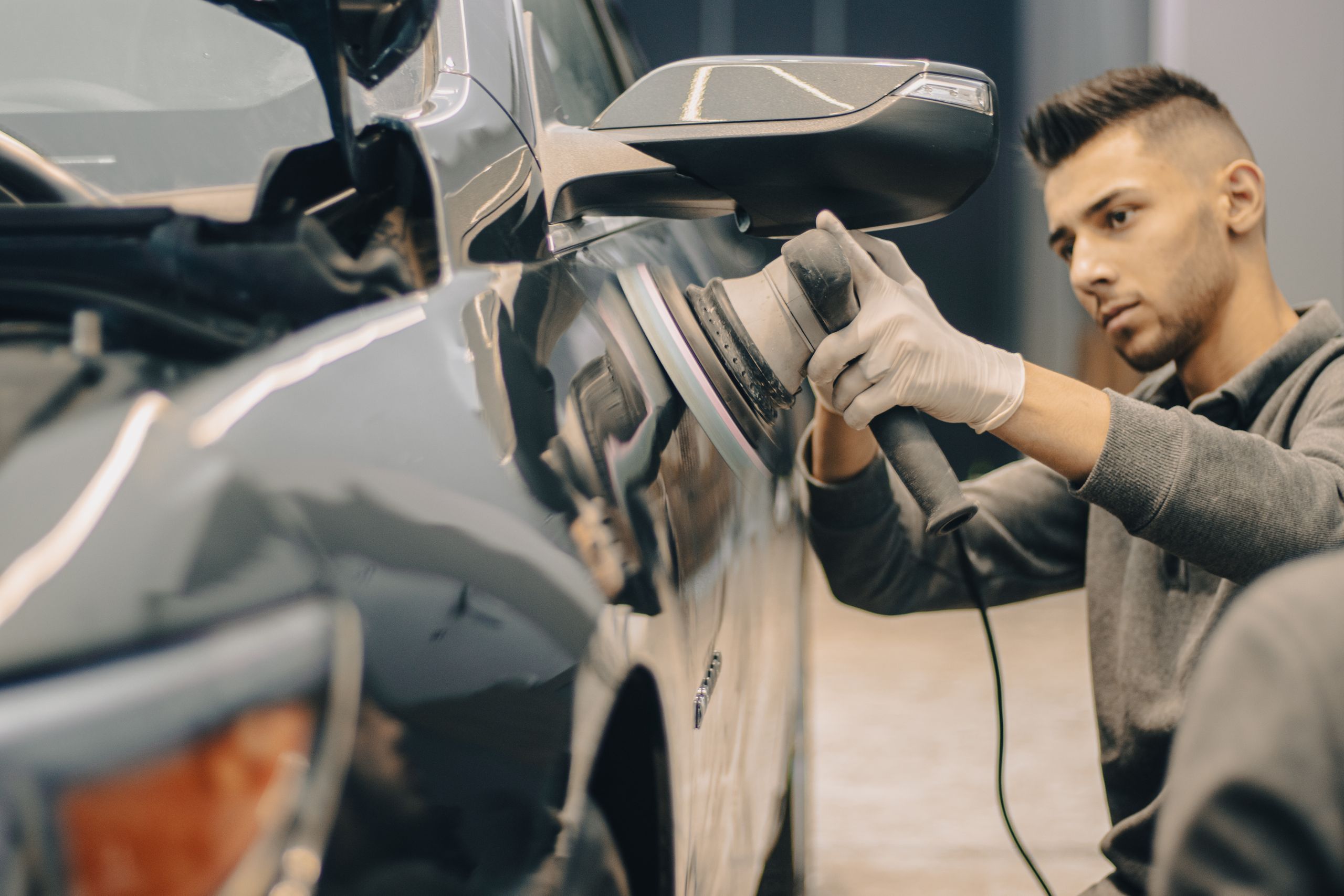 A technician machine-sanding a car door panel to prepare it for paint