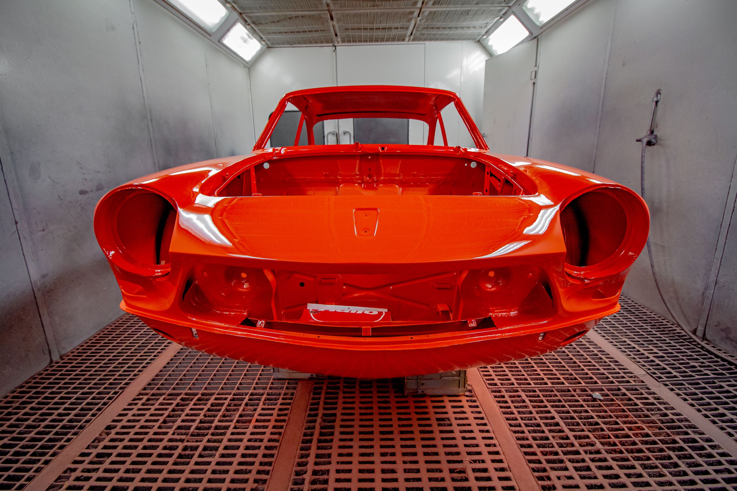 A bare red car body shell under the lights of a paint booth
