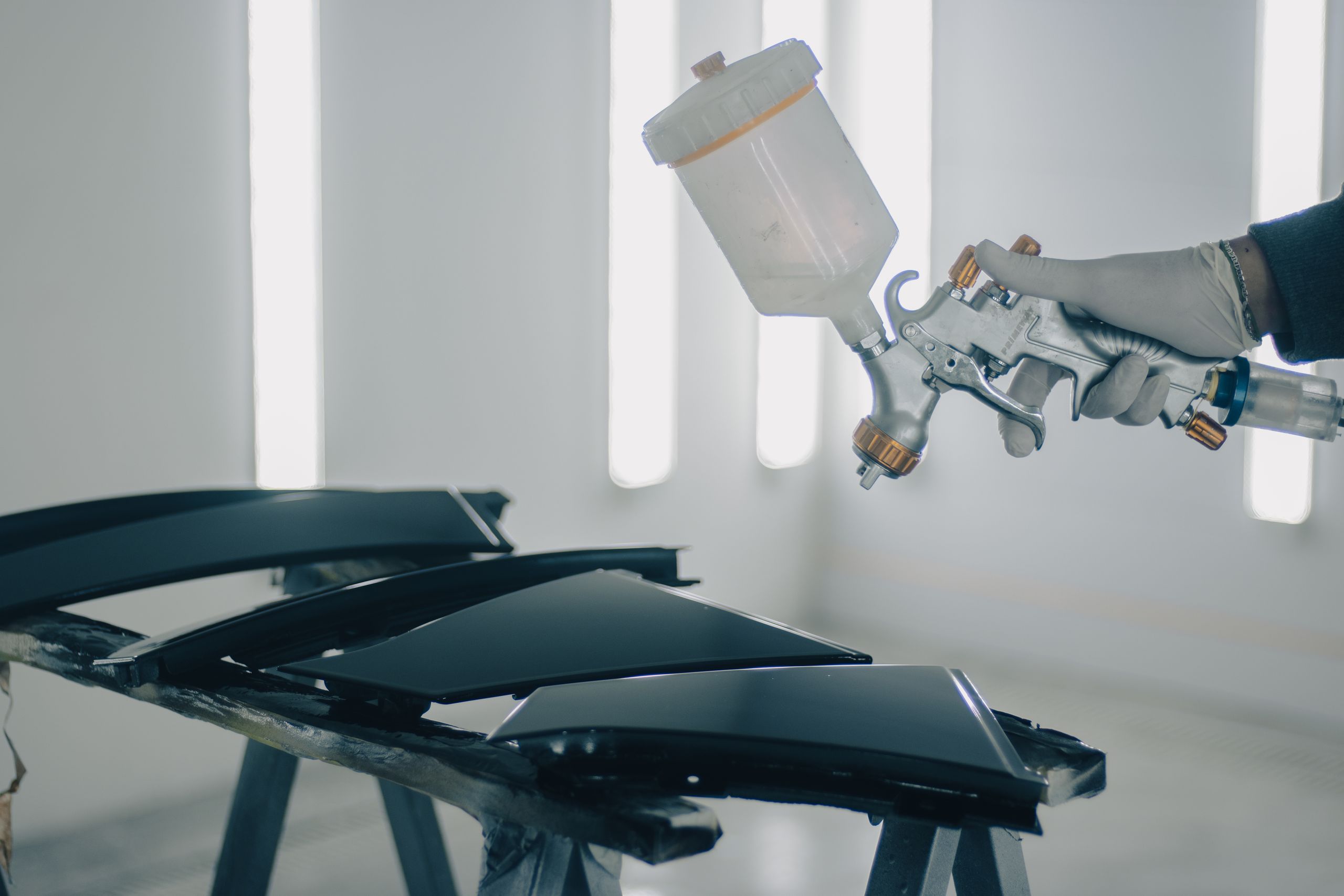 A spray gun laying down paint on body panels in a paint booth