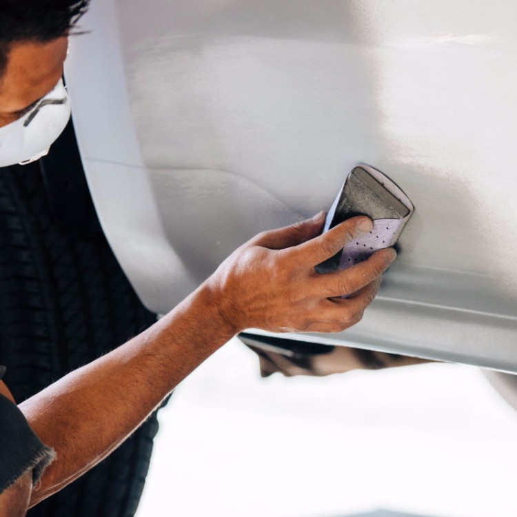 Hand-sanding a white body panel at Doug's Auto Body